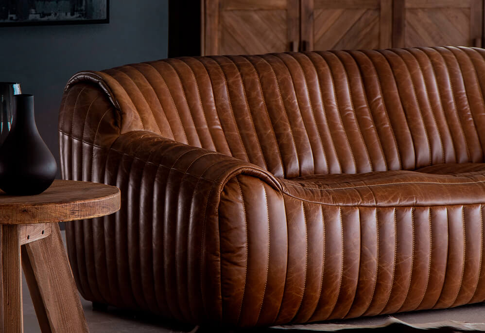 Close up of brown leather panelled couch and round wooden side table